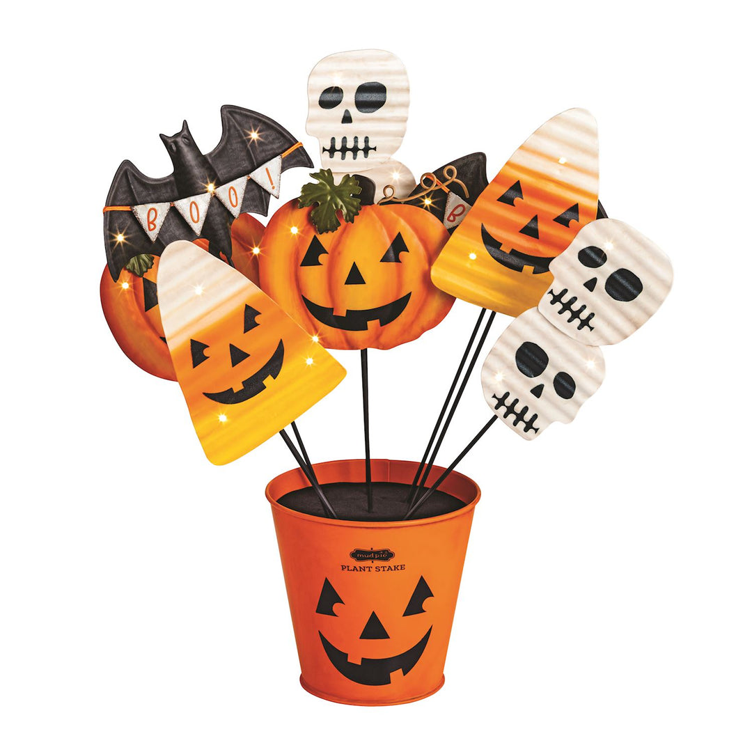 Halloween-themed plant stakes with pumpkins, bats, and skulls in an orange pot on a white background.