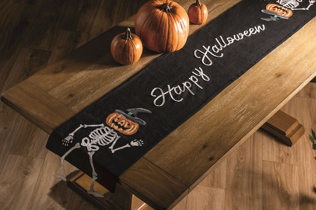Black Happy Halloween Table Runner wtih Jack-o-lantern skeletons on a wood table.