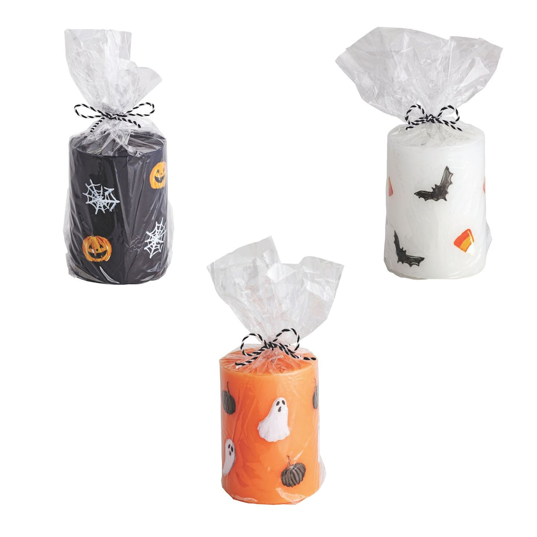 Three handpainted Halloween pillar candles in white, black, and orange colors with decorative elements suited for the Halloween theme, each with a white ribbon on top.
