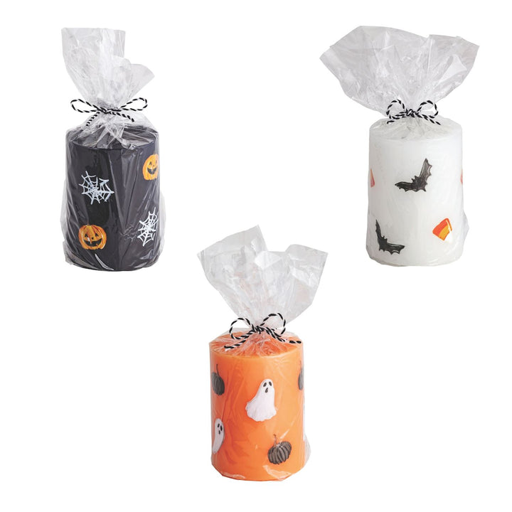 Three handpainted Halloween pillar candles in white, black, and orange colors with decorative elements suited for the Halloween theme, each with a white ribbon on top.