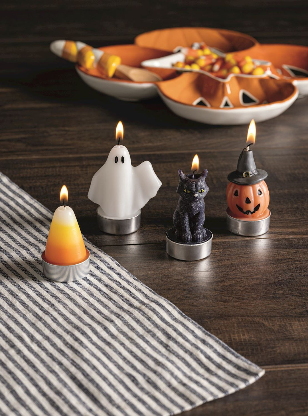 Halloween-themed candles on a wooden table with decorative pumpkins in the background.