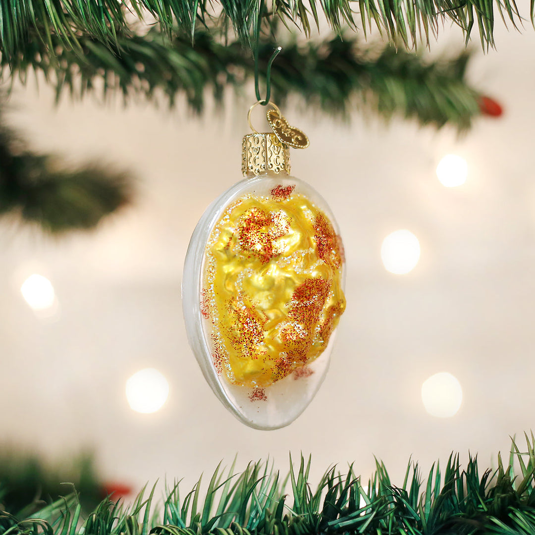 Decorative ornament that looks like a deviled egg on a Christmas tree with lights in the background.