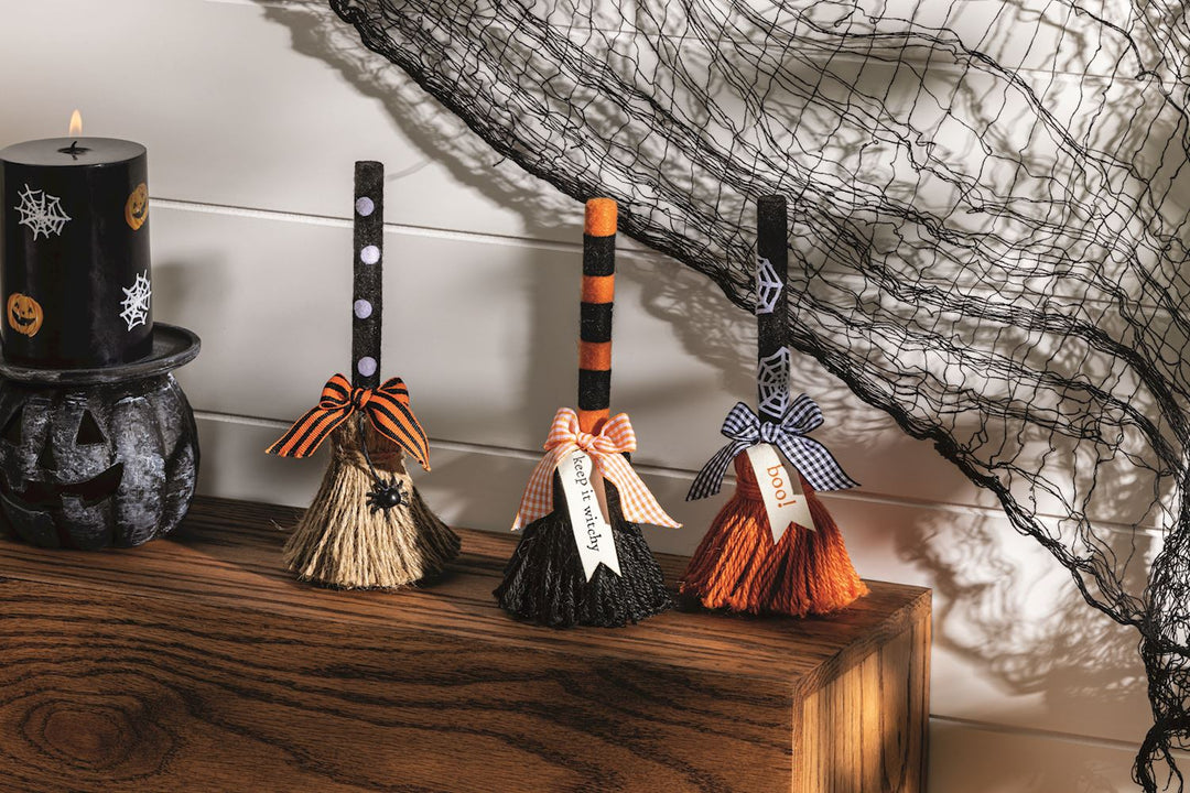Halloween-themed broom decorations on a wooden surface with a black spider web in the background.
