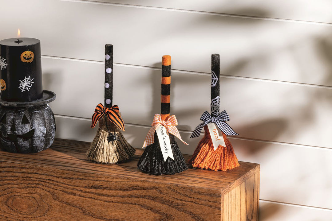 Four decorative brooms with Halloween-themed decorations on a wooden surface.