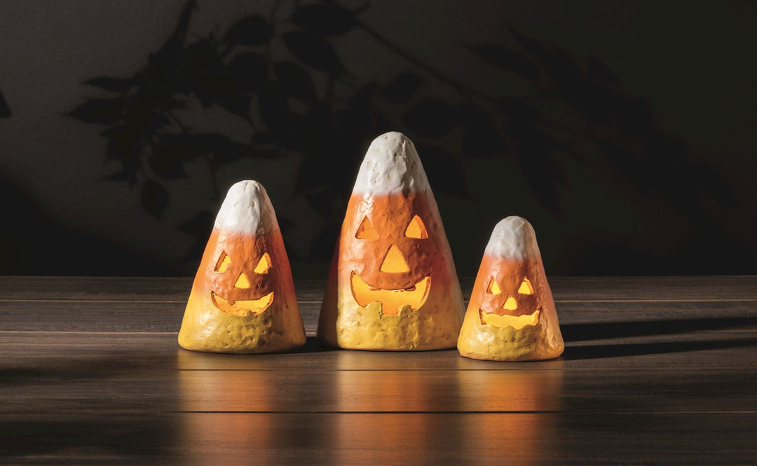 Three candy corn-shaped Halloween lanterns with glowing faces on a wooden surface.